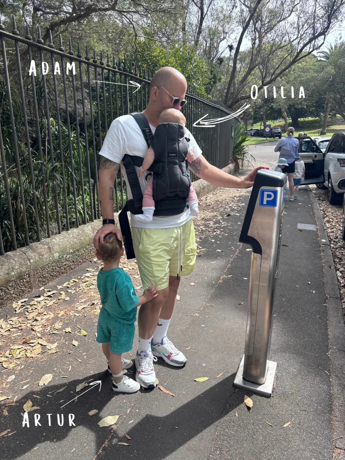 Adam on a walk through a Sydney park, carrying Otília and holding hands with Artur